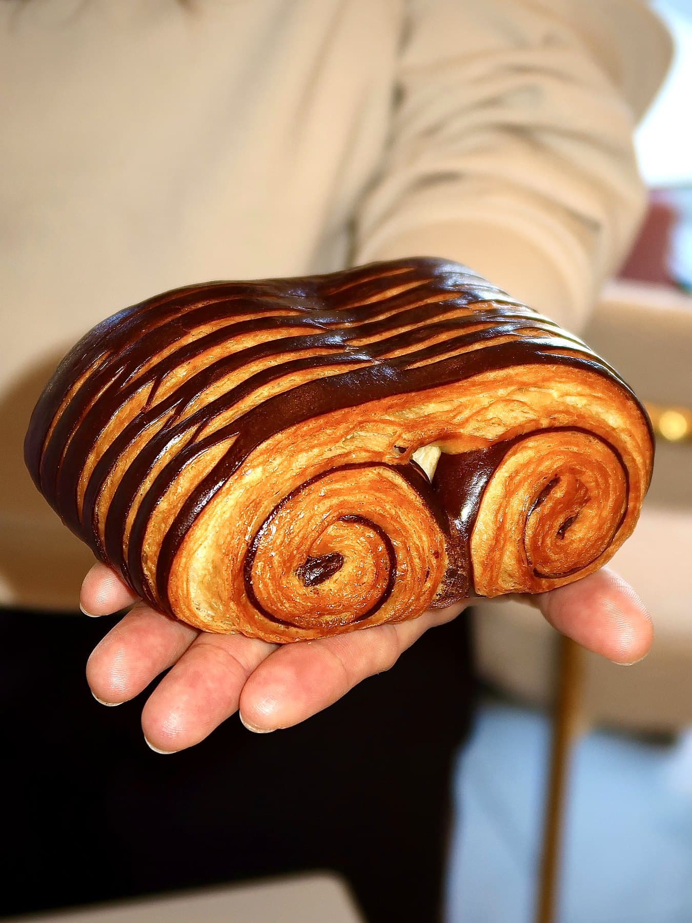 A two-tone chocolate-striped croissant held in two hands