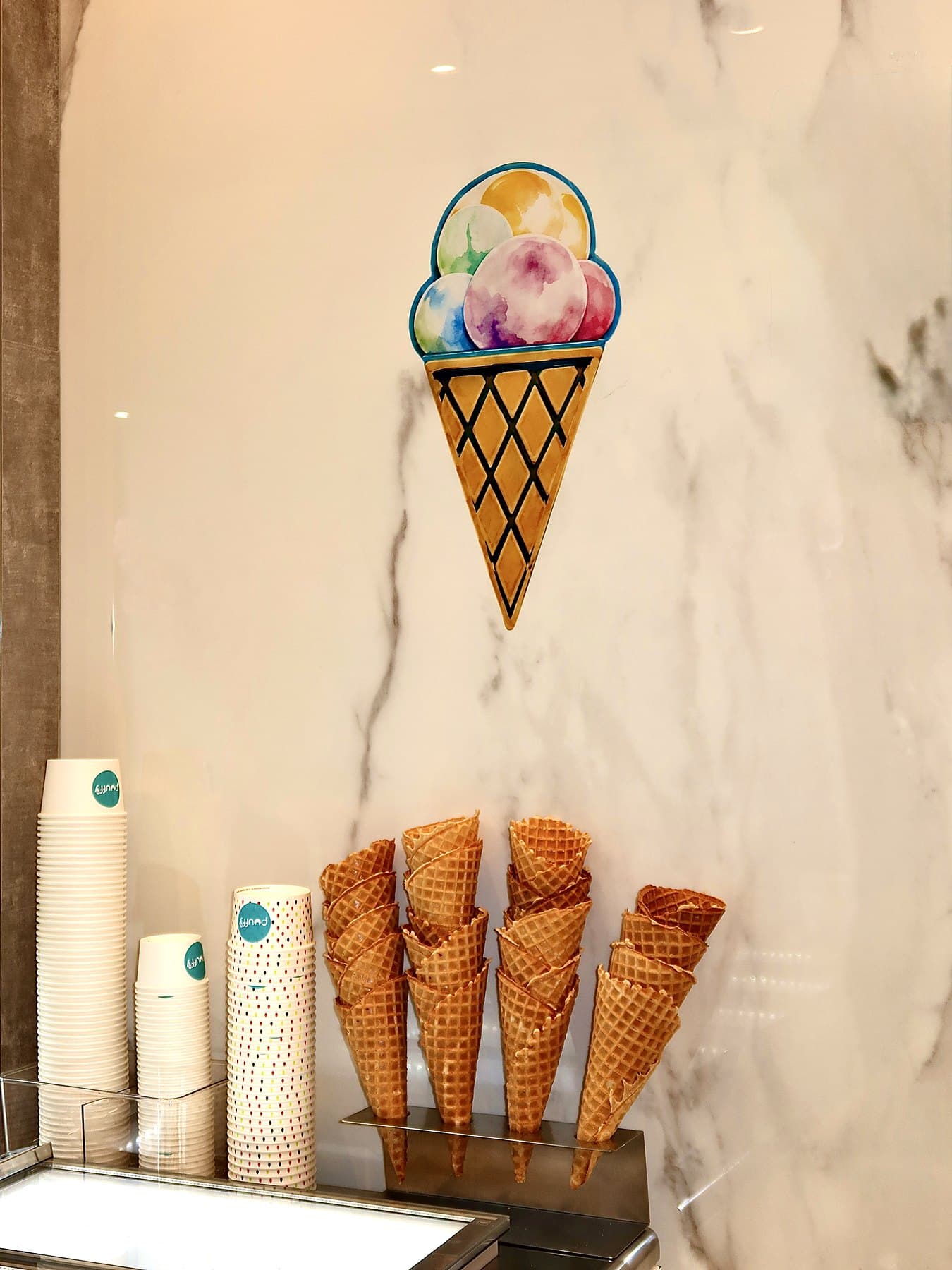 The ice cream counter with a stack of waffle cones and the Puuffy cone sign on marble