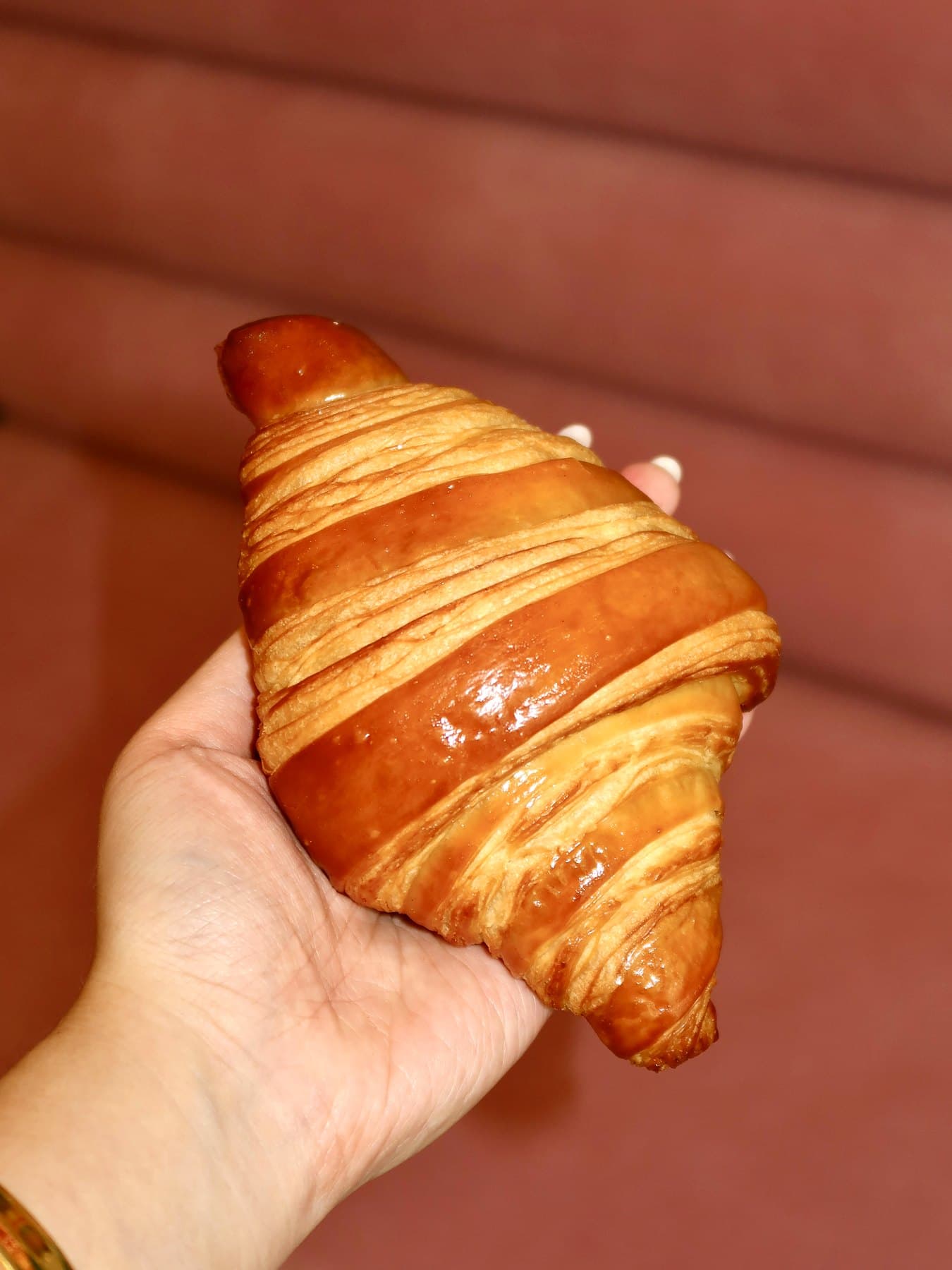 A golden croissant held up against a pink banquette