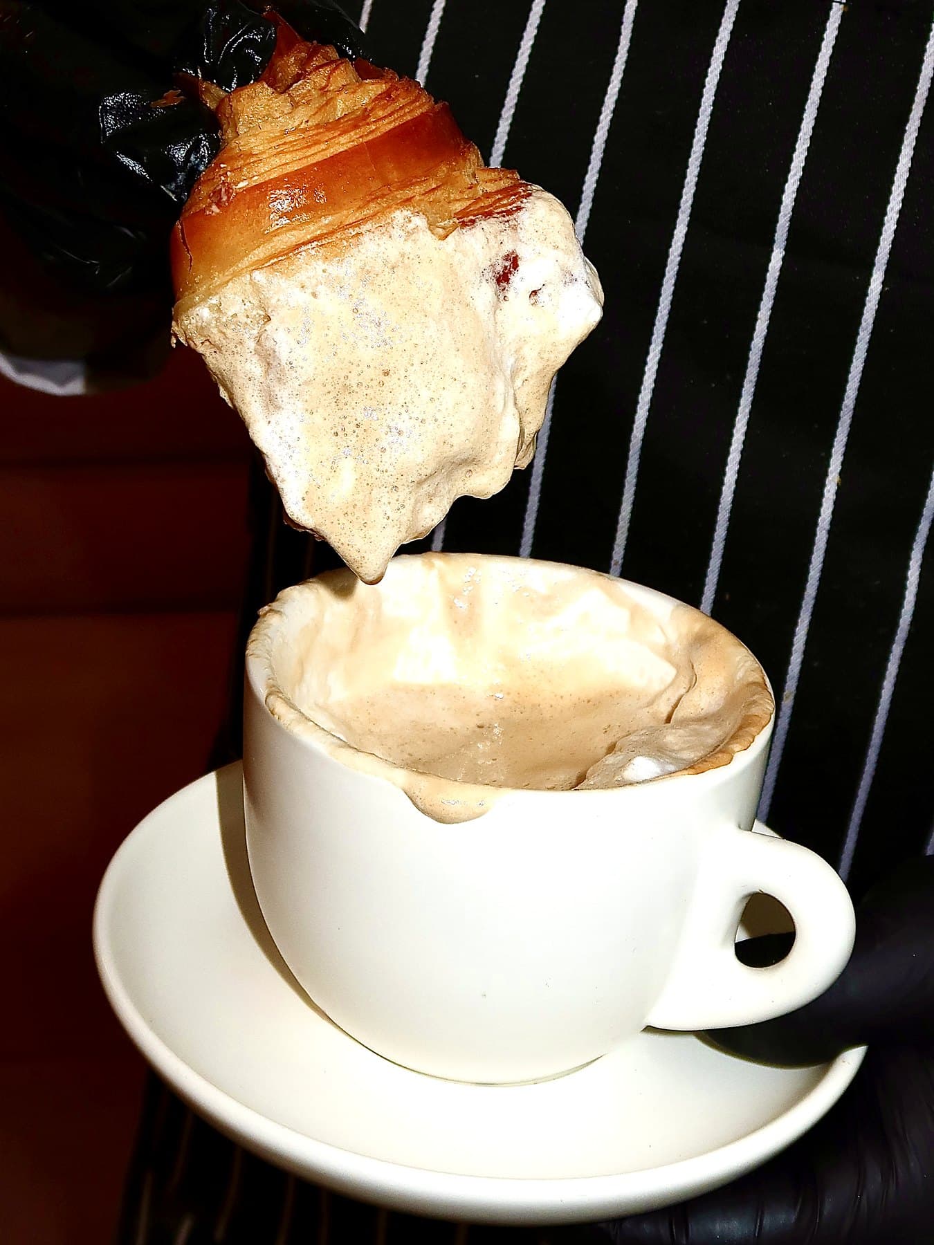 A croissant dipped into a cup of coffee topped with ice cream